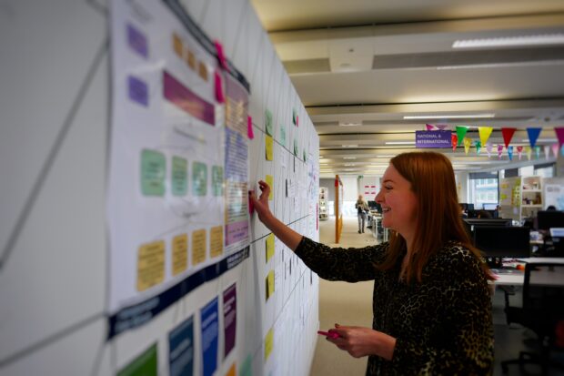 A picture of Georgie Baker putting a post it note on a poster of the bigger picture.