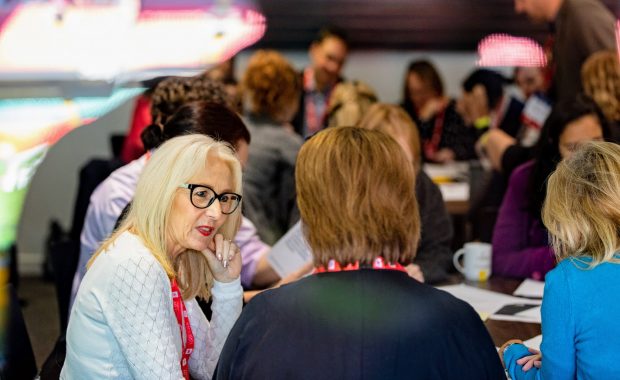 A group of people in a workshop at Transforming Together in Cardiff, two women in focus, with a wider group at another table in the background