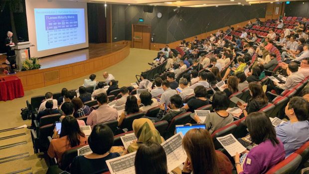 A lecture hall at the Civil Service College in Singapore - rows of students are looking at printouts of the 7 Lenses Maturity Matrix, while Naomi Stanford stands on the stage, on the left of the picture, presenting the same material.